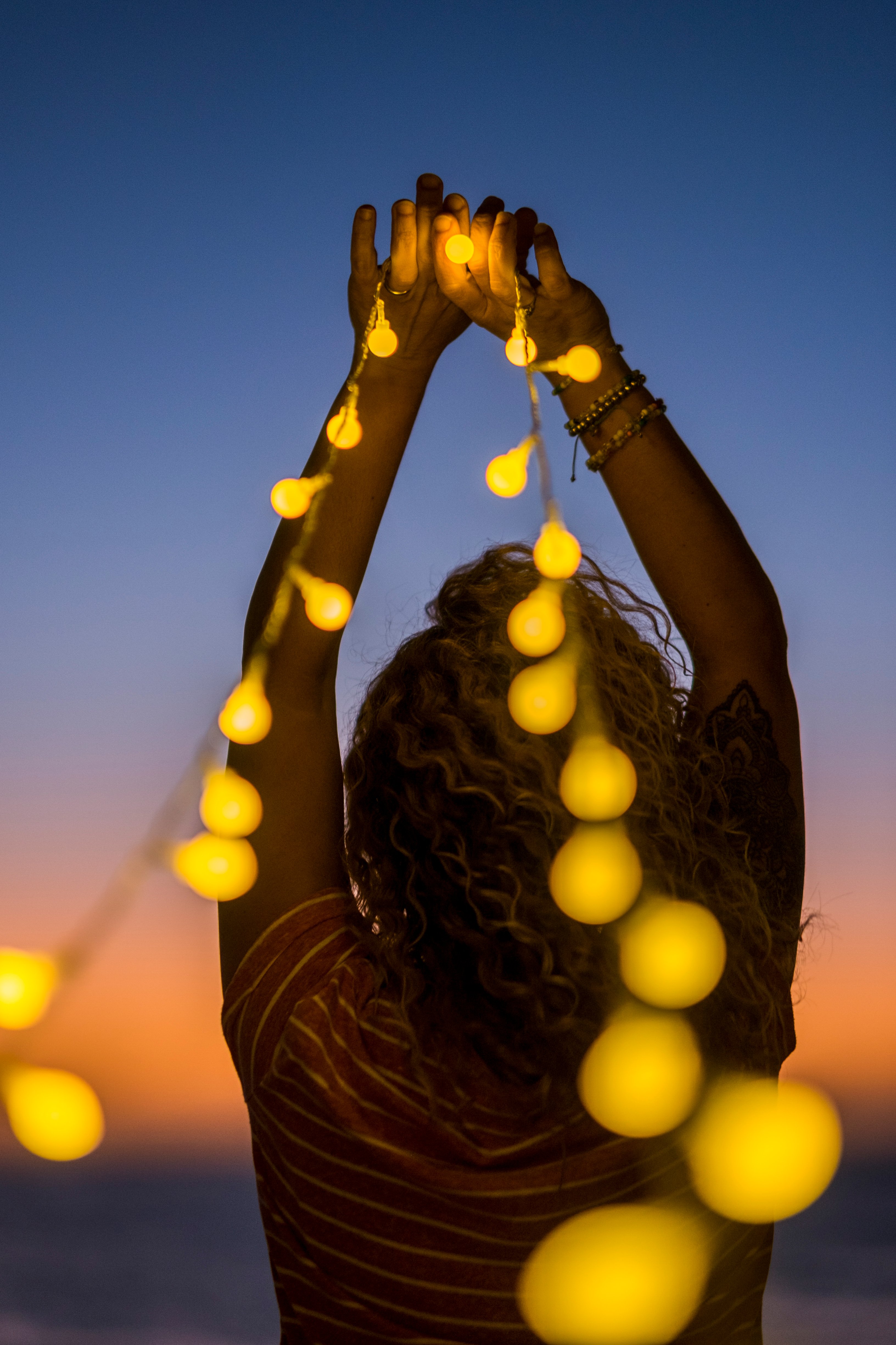 rear-view-woman-holding-illuminated-lighting-equipment-against-sky-sunset
